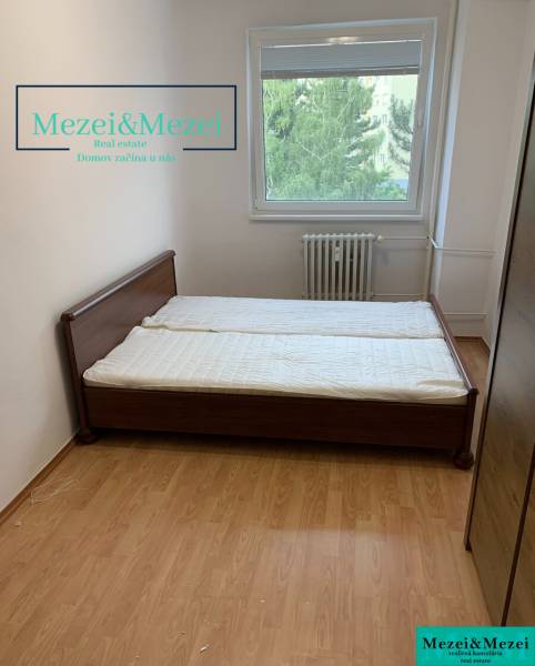 Bedroom with a bed, wooden decor flooring, window with a view of greenery.