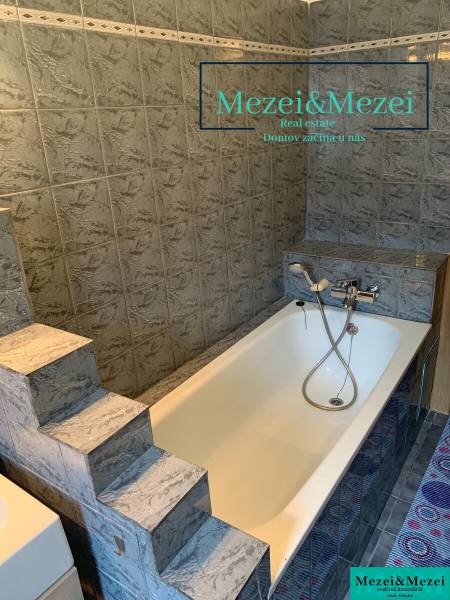 A bathroom with steps and a bathtub surrounded by gray tiles in a two-room apartment.