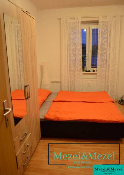 Bedroom in a two-room apartment with orange blankets, wardrobe, and lamp, floor with wooden decor.
