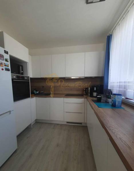 A kitchen with white cabinets, wooden decor on the floor, and a countertop in a 2-room apartment.