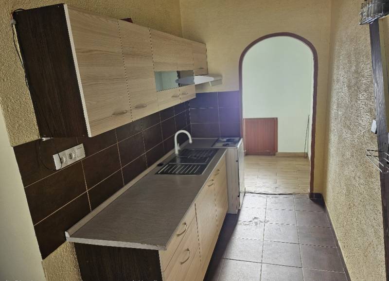 A kitchen in a 2-room apartment with brown tiles and a wooden decor floor.