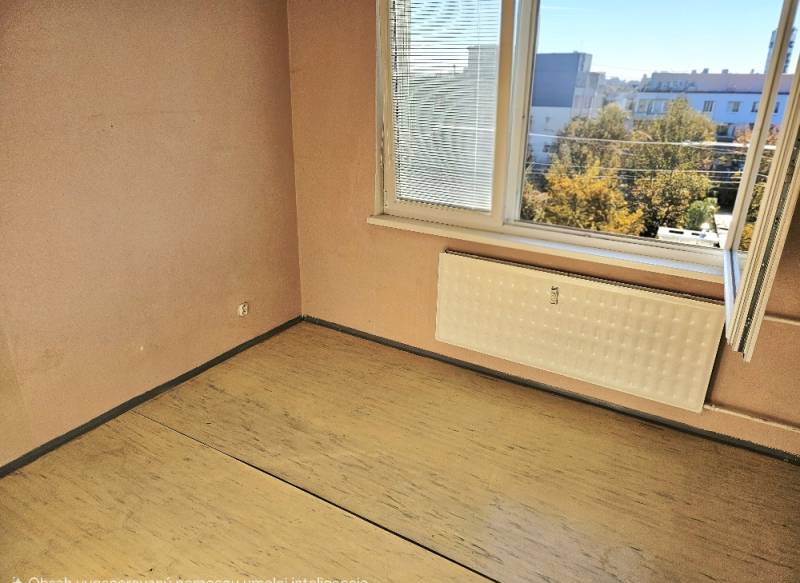 A room in a 2-room apartment with a window, a wooden decor floor, and a radiator.