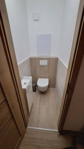 Bathroom with a wall-hung toilet and a floor with a wooden decor in a 2-room apartment.
