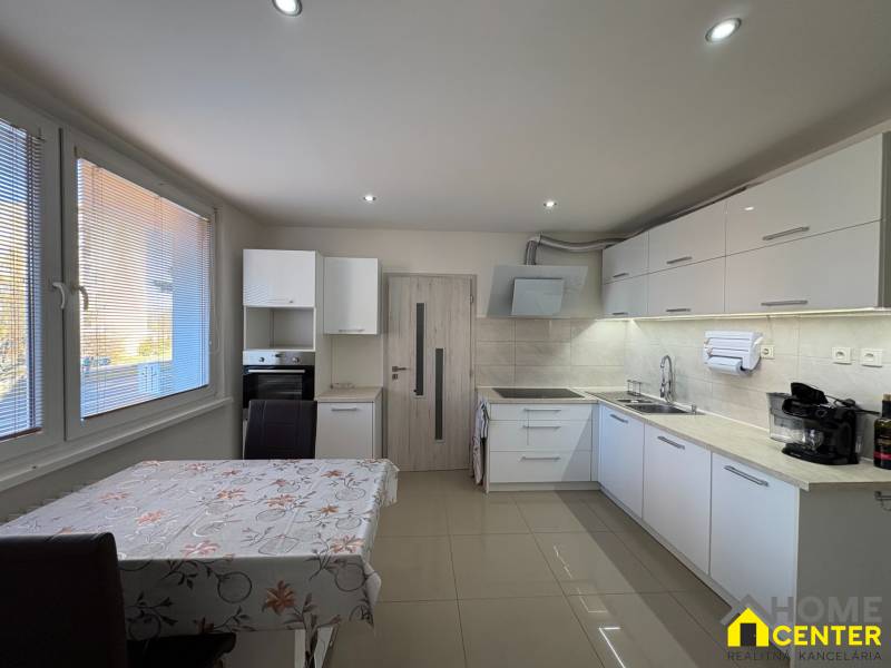 A kitchen in a 3-room apartment with white cabinets and tiles, and a floor with a wooden design.