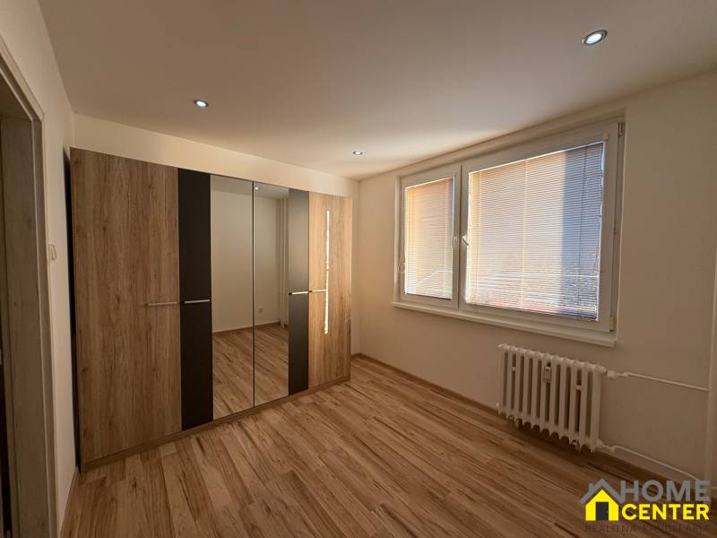 A bedroom in a three-room apartment with a wooden decor floor and a built-in wardrobe.