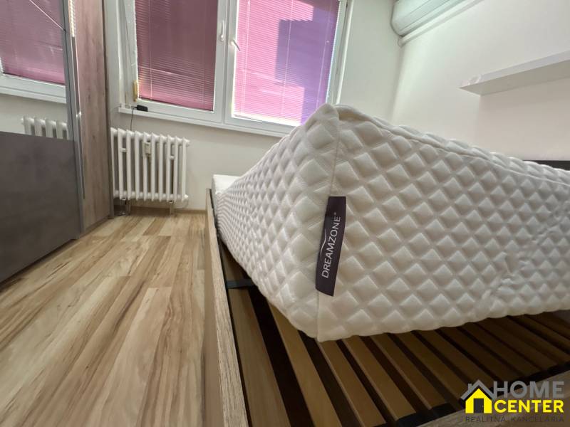 A bedroom with wood-patterned flooring, a quality mattress, and a large radiator in a 3-room apartment.