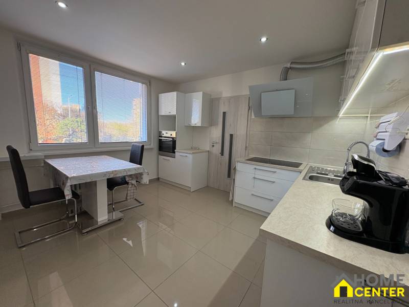 The kitchen of a 3-room apartment with large windows, a dining table, and light flooring.
