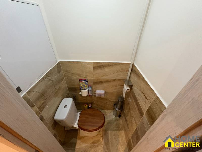 A toilet with wall tiles and flooring with a wood decor in a 3-room apartment.