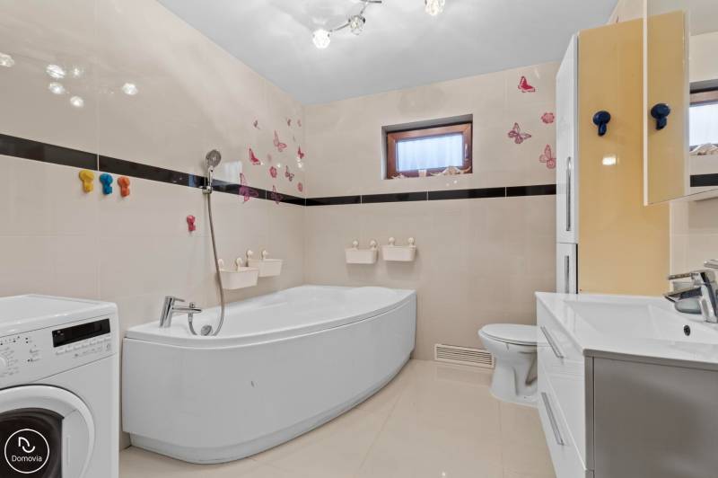 A bathroom in a family house with a bathtub, sink, washing machine, and butterfly motifs on the walls.