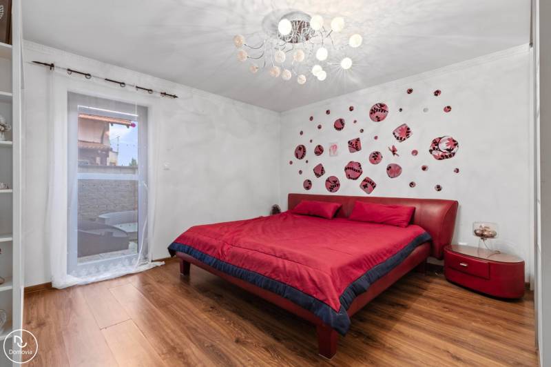Bedroom with a red bed, wall decoration, and wooden decor flooring in a family house.