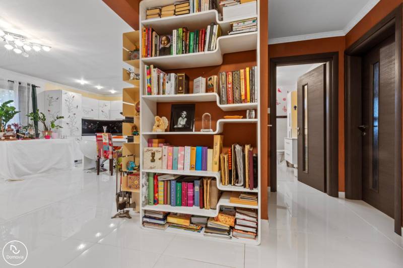 Library with diverse books, white floor, and plants in a family house.