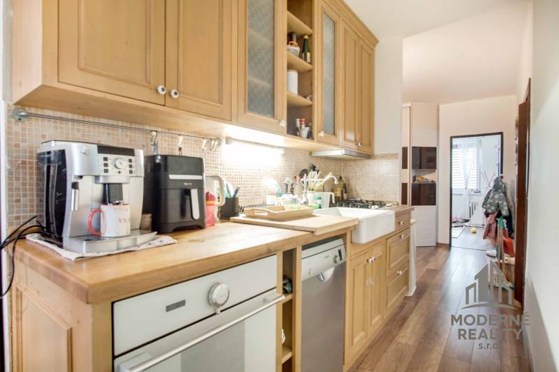 A kitchen of a 3-room apartment with wooden kitchen cabinets and a floor with a wood design.