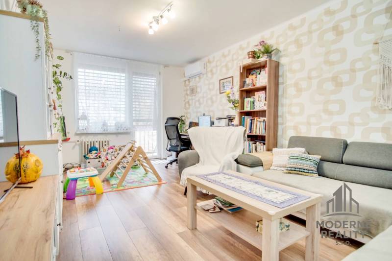 Living room in a three-room apartment with a comfortable sofa, children's corner, and wooden decor flooring.