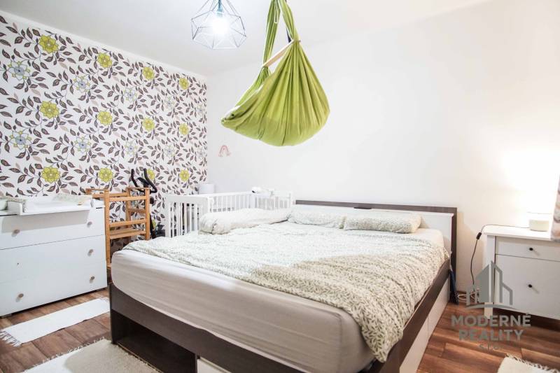 A bedroom with patterned wallpaper and a green swing in a 3-room apartment.