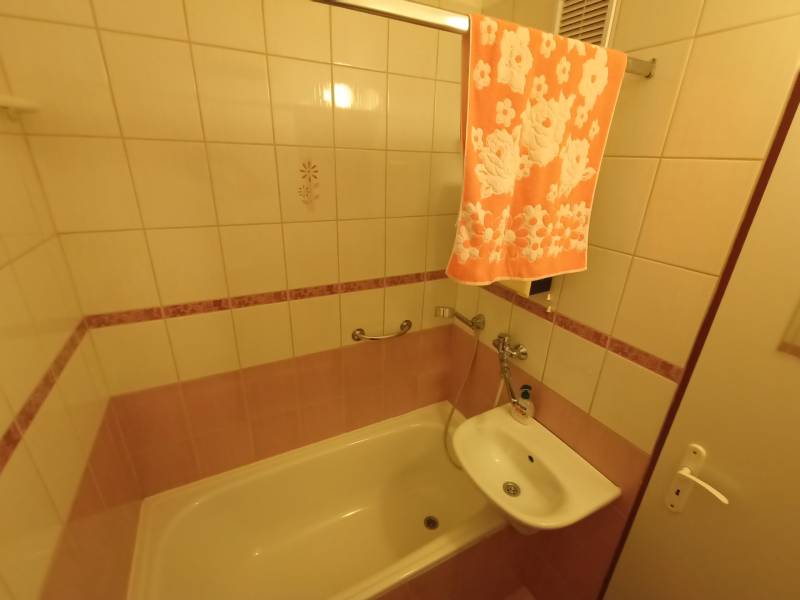 Bathroom of a two-room apartment with a shower, sink, and towel in warm shades.