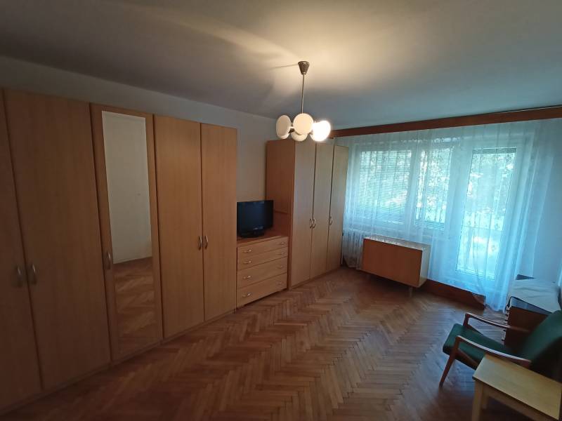 A room in a 2-room apartment with wardrobes, a television, and a floor with a wooden decor.