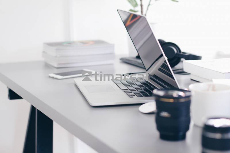 A laptop on the desk in an office with books and a mug.