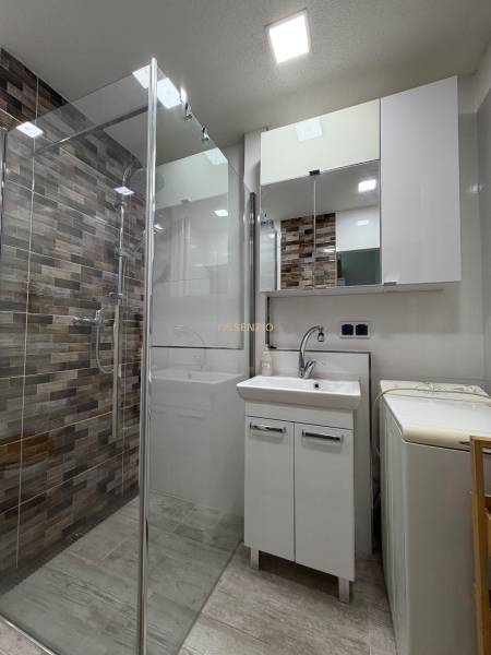 A bathroom in a 2-room apartment with a shower, sink, and washing machine.
