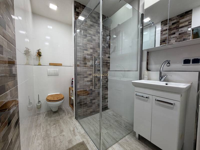 Bathroom in a 2-room apartment with a brick shower corner and a floor with a wooden decor.