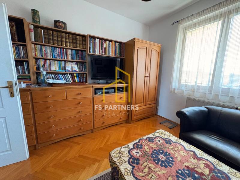 A room in a multi-room apartment with a library, a television, and a floor with a wooden decor.