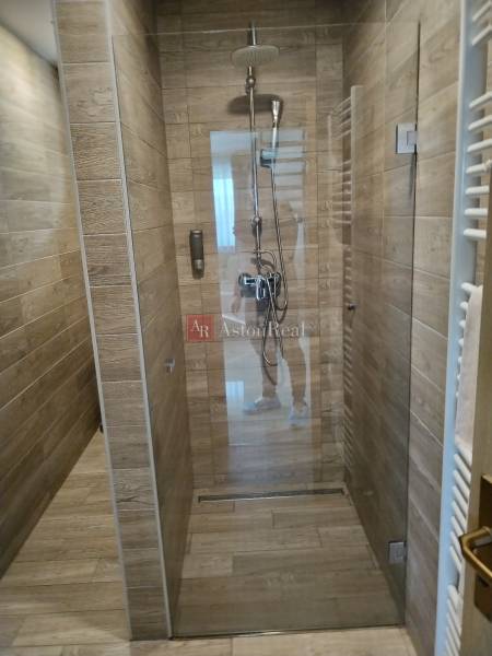 Shower corner with ceramic tiles and a wooden decor floor in a cottage.