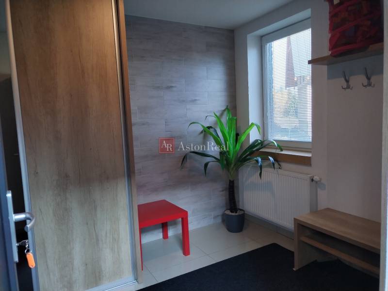 Interior of a cabin with a red table, a plant, a radiator, and a wall with wooden decor.