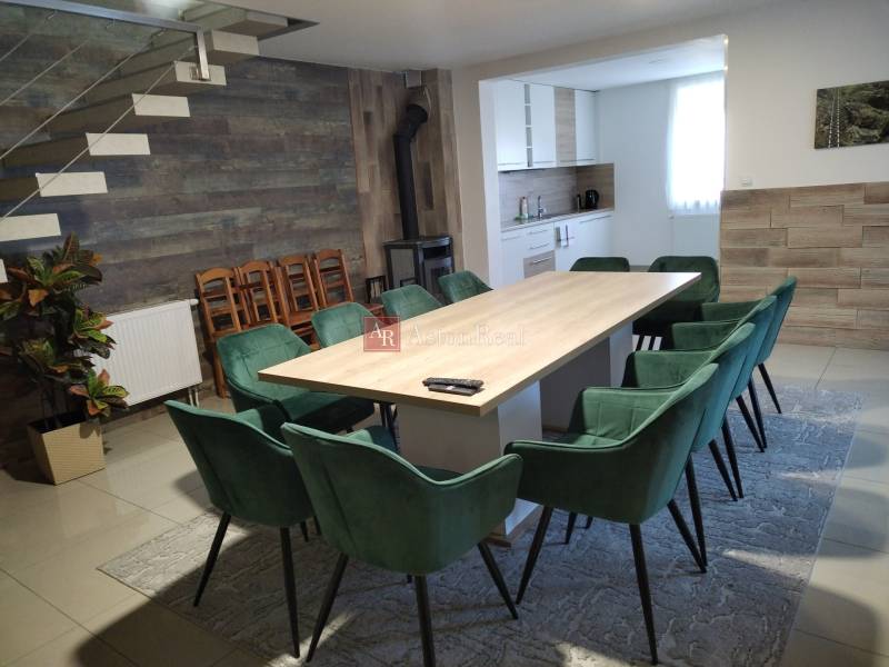 Dining room in a cottage with a large table, modern chairs, and a kitchenette.