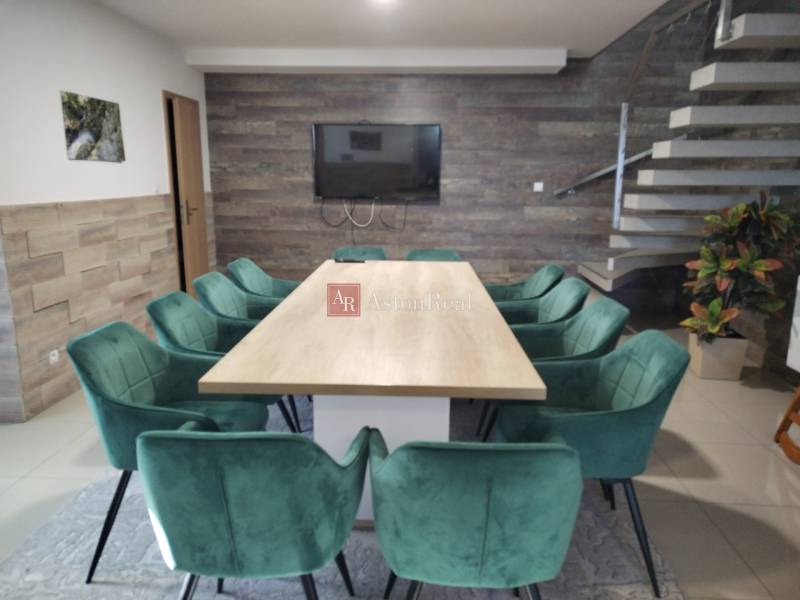 A dining room in a cabin with wooden decor, a staircase, and green chairs around the table.