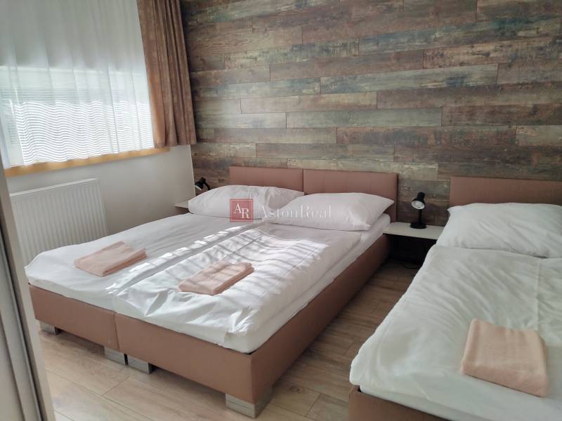 A room in a cottage with two beds, a wooden wall, and a floor with a wooden decor.