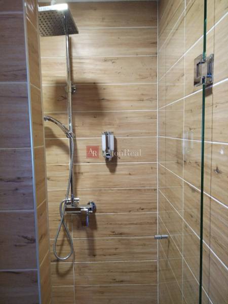 Shower corner in a cabin with wood-patterned tiles, large rain shower.