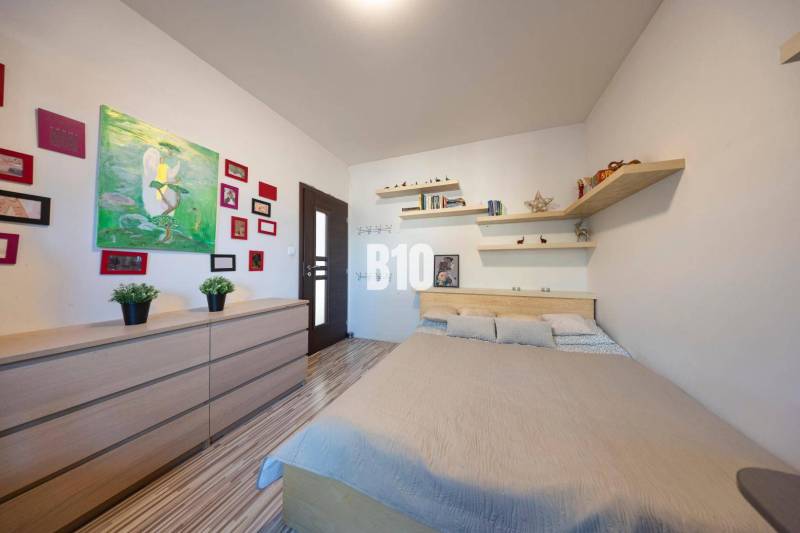 Bedroom in a family house with a bed, shelves, paintings, and a wooden decor floor.