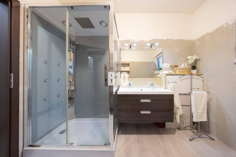 A bathroom in a family house with a wooden decor floor, a shower corner, and a mirror.