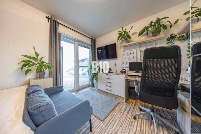 Office in a family house with a sofa, desk, television, and plants.