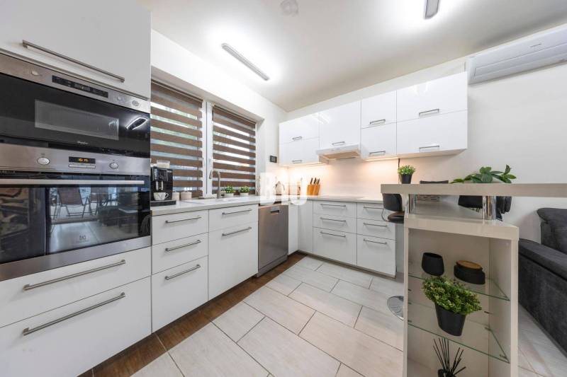 A kitchen in a family house with white cabinets and a window with blinds.