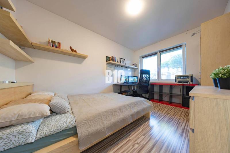 A bedroom in a family house with a desk, shelves, and a wooden decor floor.