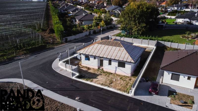 A family house under construction in Horné Štitáre with surrounding buildings and an asphalt road.