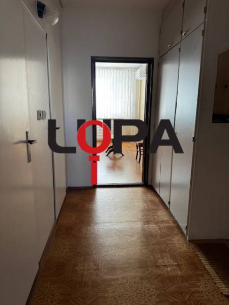 A hallway in a 3-room apartment with a wooden decor floor leading to a bright room.