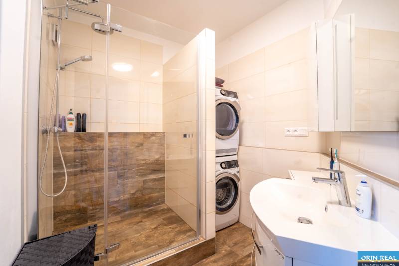Bathroom with a shower, washing machine, and dryer, 3-room apartment, floor with wood decor.