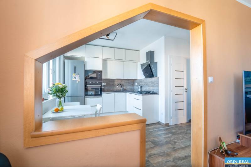 A kitchen in a 3-room apartment with modern appliances and a wooden decor floor.