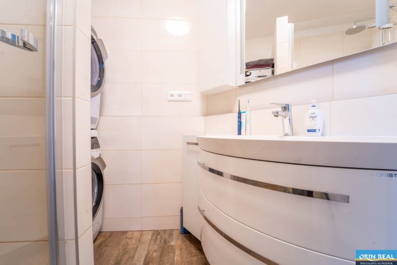 Bathroom with a washing machine and dryer in a 3-room apartment with a wooden decor floor.