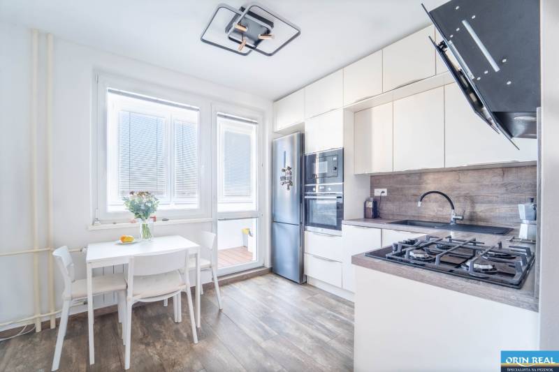 A kitchen in a 3-room apartment with a wooden decor floor and light furniture.