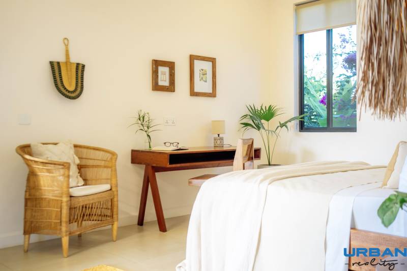 A bright bedroom in a family house with a rattan chair and a wooden table.