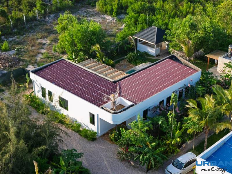 Construction of houses in Paje, Unguja South Region, with red roofs surrounded by greenery.
