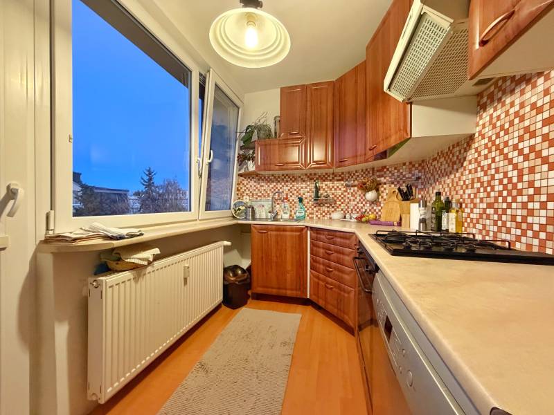 A kitchen in a 3-room apartment with light furniture and a wooden decor floor.