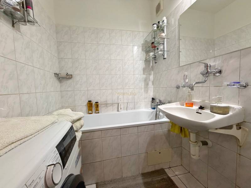 Bathroom in a 3-room apartment with a washing machine, sink, and bathtub, tiled with light tiles.