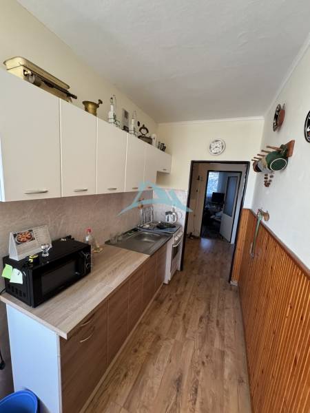 A kitchen in a 3-room apartment with a wood-patterned floor, appliances, and storage cabinets.