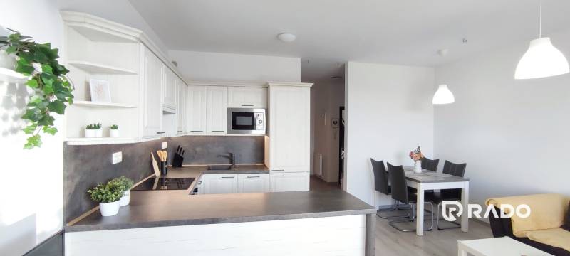 Kitchen of a 2-room apartment with white cabinets and a dining table, floor with wooden decor.