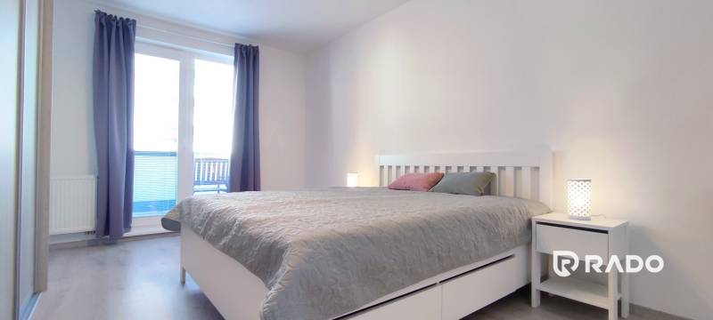 A bedroom in a two-room apartment with light furniture and a wooden decor floor.
