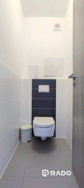 A toilet with white tiles and a wall-hung toilet bowl in a 2-room apartment.