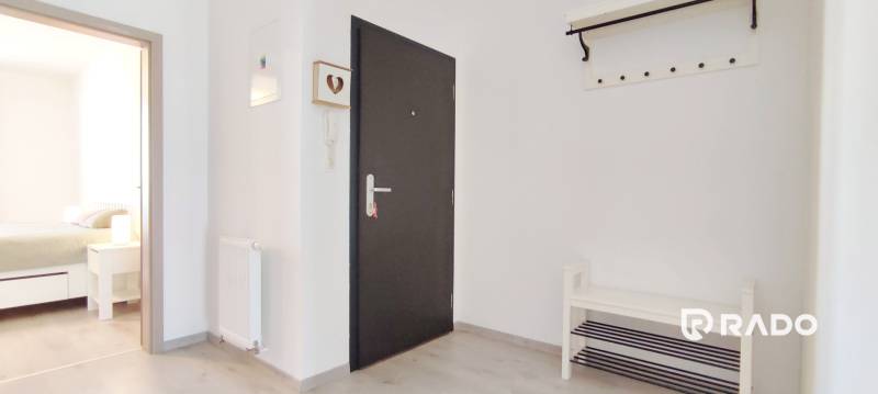 An entrance hallway with light walls and a wooden decor floor leads to the bedroom.